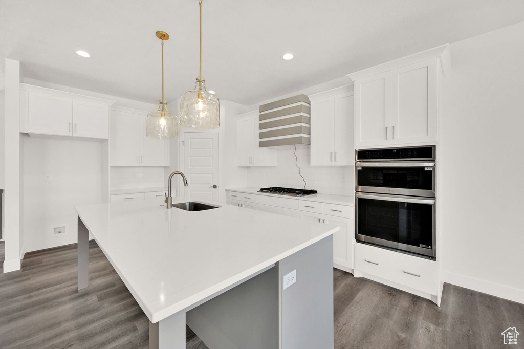 Kitchen with decorative backsplash, dark hardwood / wood-style floors, an island with sink, sink, and double oven