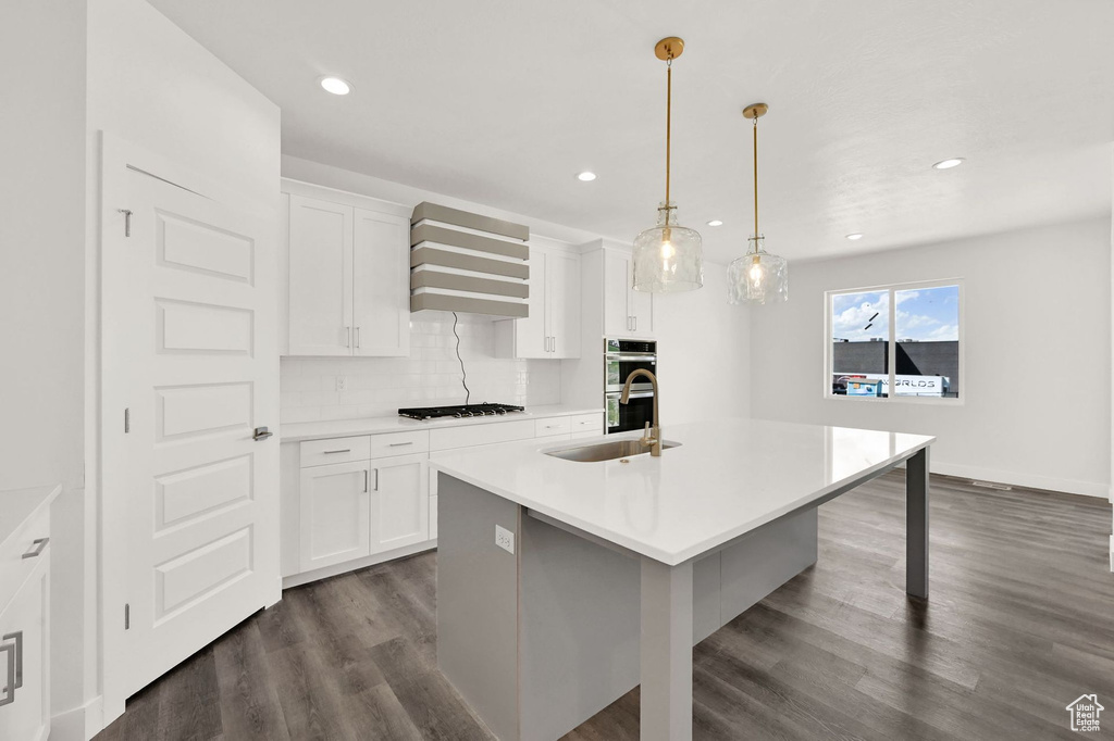 Kitchen with white cabinetry, dark hardwood / wood-style floors, decorative backsplash, and a center island with sink