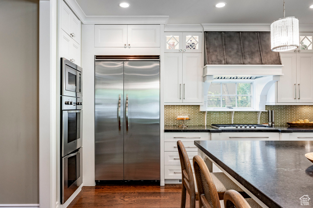 Kitchen featuring white cabinets, tasteful backsplash, dark hardwood / wood-style floors, pendant lighting, and built in appliances