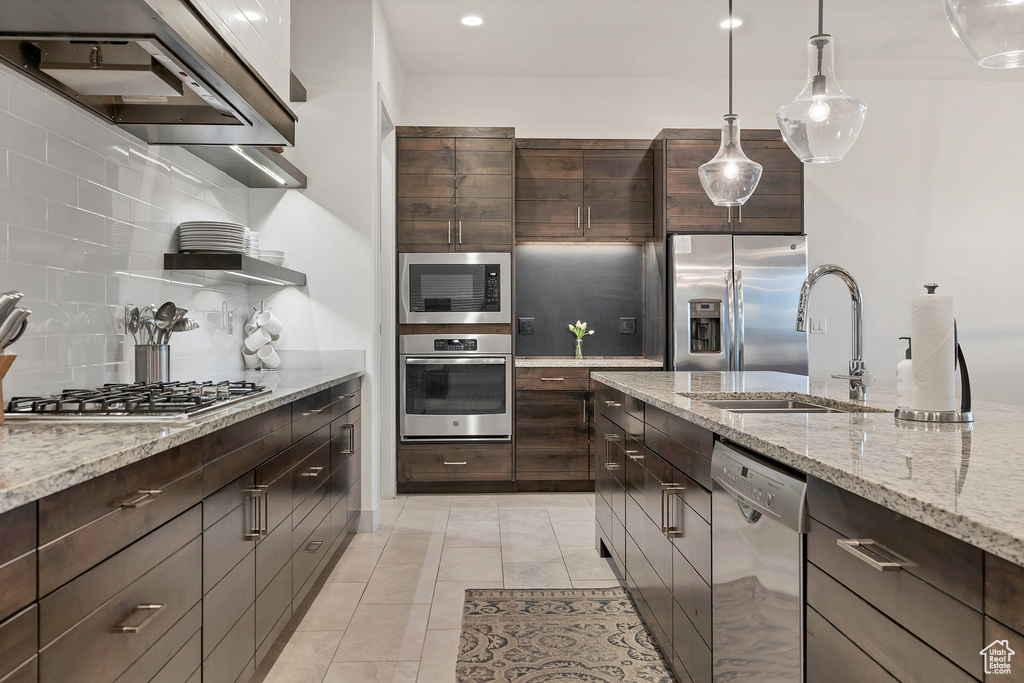Kitchen with light stone countertops, appliances with stainless steel finishes, premium range hood, tasteful backsplash, and pendant lighting