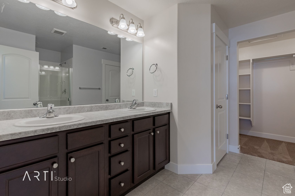 Bathroom with dual sinks, vanity with extensive cabinet space, an enclosed shower, and tile floors