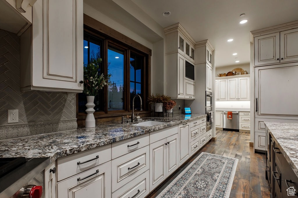 Kitchen with dark hardwood / wood-style floors, light stone countertops, tasteful backsplash, sink, and white cabinetry