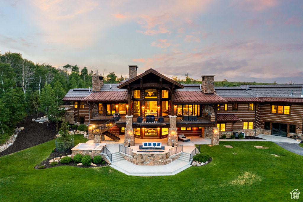 Back of house featuring a chimney, a standing seam roof, a patio, and stone siding