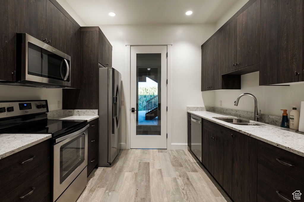 Kitchen featuring light stone countertops, dark brown cabinets, light wood-type flooring, appliances with stainless steel finishes, and sink