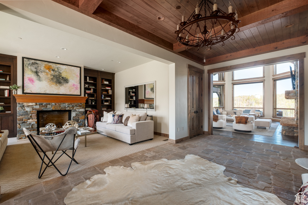 Living area featuring a wooden ceiling with exposed beams, stone finish floors, a chandelier, a fireplace, and built in features
