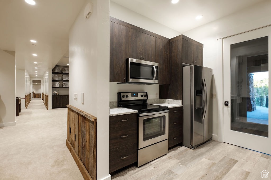 Kitchen with appliances with stainless steel finishes, light stone countertops, dark brown cabinetry, and light colored carpet