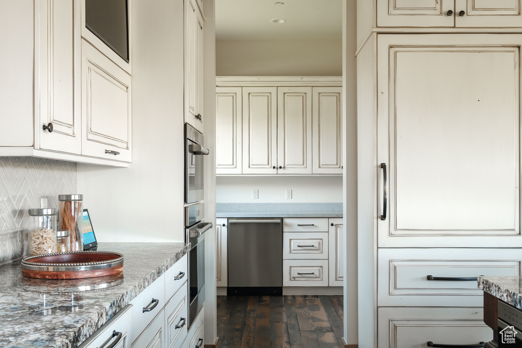 Kitchen featuring cream cabinetry, stainless steel appliances, dark wood finished floors, backsplash, and light stone countertops