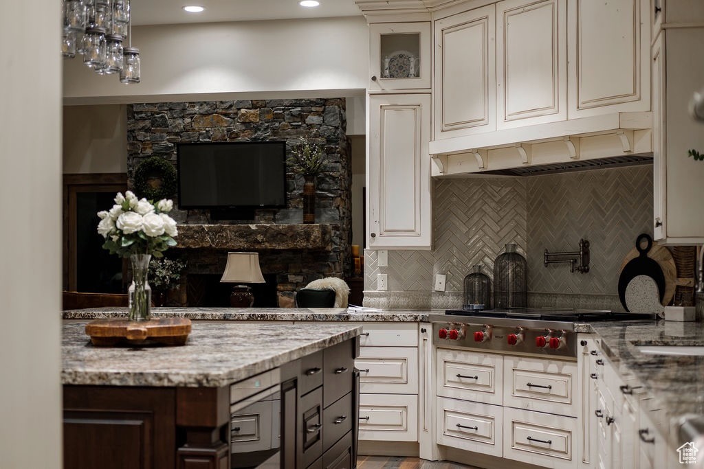 Kitchen featuring custom exhaust hood, light stone countertops, tasteful backsplash, and stainless steel gas cooktop