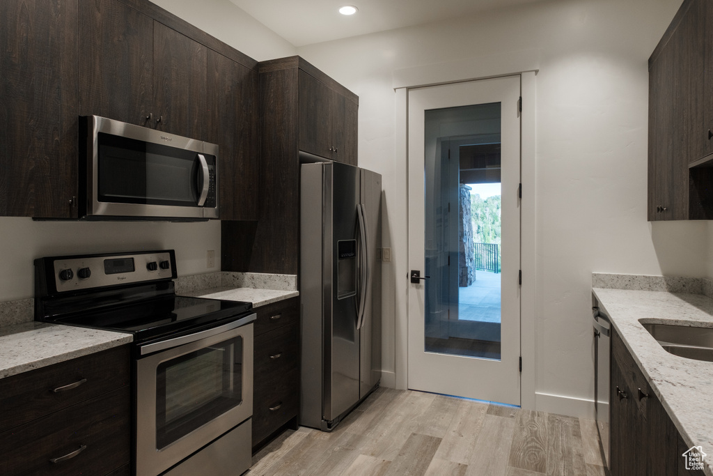 Kitchen featuring stainless steel appliances, light wood-style flooring, dark brown cabinetry, light stone countertops, and recessed lighting