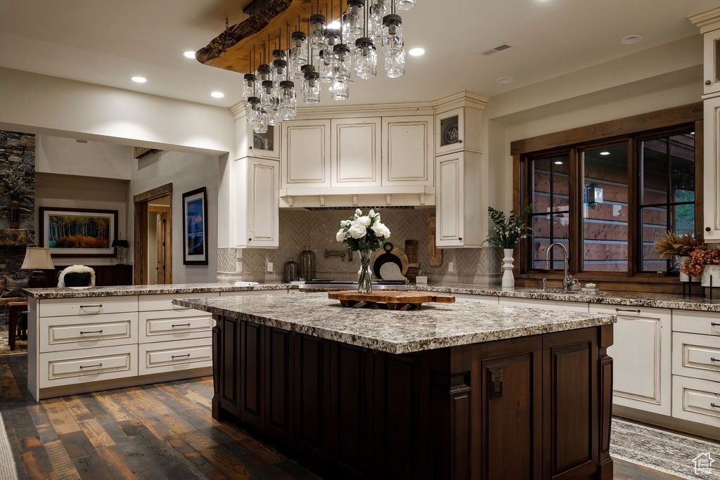 Kitchen with backsplash, a center island, dark wood-type flooring, sink, and pendant lighting