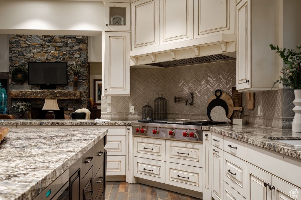 Kitchen featuring light stone countertops, tasteful backsplash, stainless steel gas stovetop, custom range hood, and dark hardwood / wood-style flooring