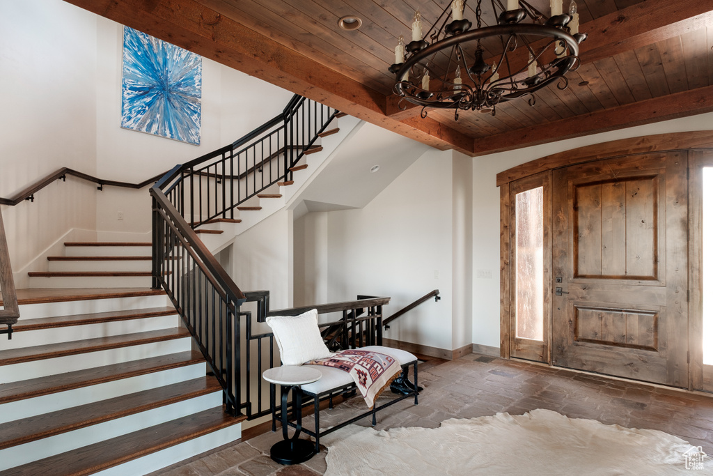 Foyer entrance with a chandelier, a wooden ceiling with exposed beams, stone tile floors, and stairway