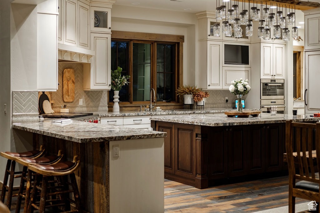 Kitchen with tasteful backsplash, wood-type flooring, double oven, and pendant lighting