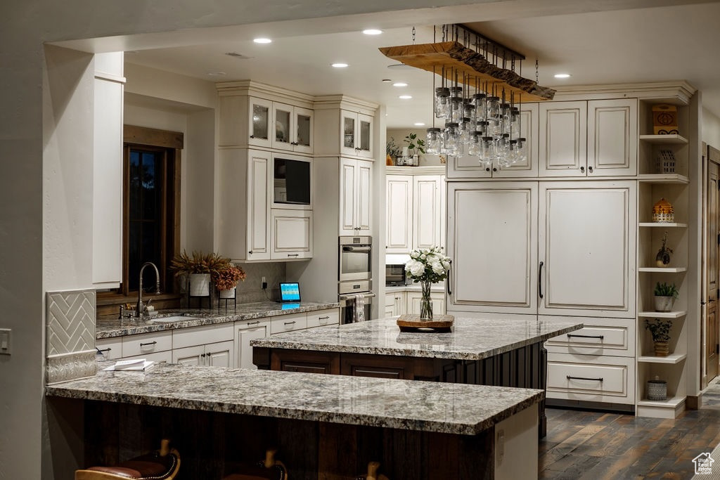 Kitchen featuring dark hardwood / wood-style flooring, light stone counters, a kitchen island, backsplash, and sink