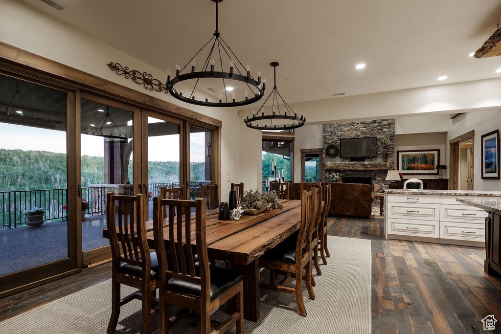 Dining room featuring a stone fireplace, a notable chandelier, and dark hardwood / wood-style flooring