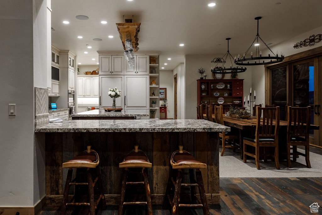 Kitchen with cream cabinets, kitchen peninsula, hardwood / wood-style floors, light stone countertops, and pendant lighting