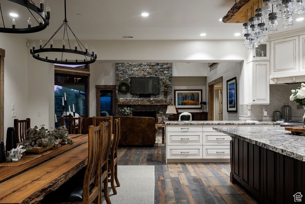 Kitchen featuring light stone countertops, dark wood-type flooring, backsplash, pendant lighting, and a stone fireplace