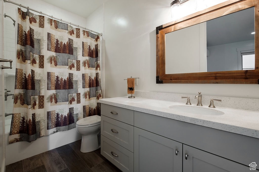 Full bathroom with hardwood / wood-style flooring, shower / bath combo with shower curtain, toilet, and vanity