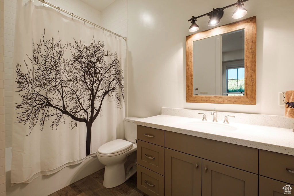 Full bathroom with vanity with extensive cabinet space, shower / bath combination with curtain, hardwood / wood-style flooring, and toilet