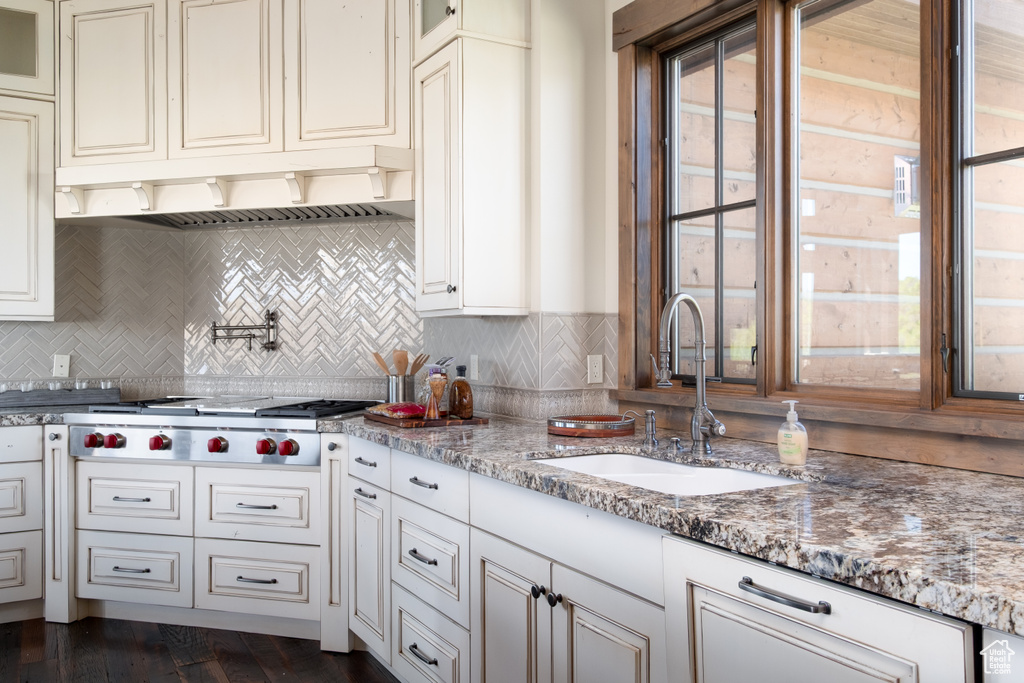 Kitchen with stainless steel gas stovetop, glass insert cabinets, under cabinet range hood, and decorative backsplash