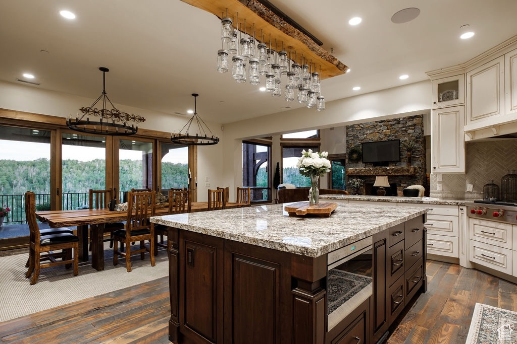 Kitchen with light stone countertops, a kitchen island, dark hardwood / wood-style flooring, dark brown cabinets, and backsplash