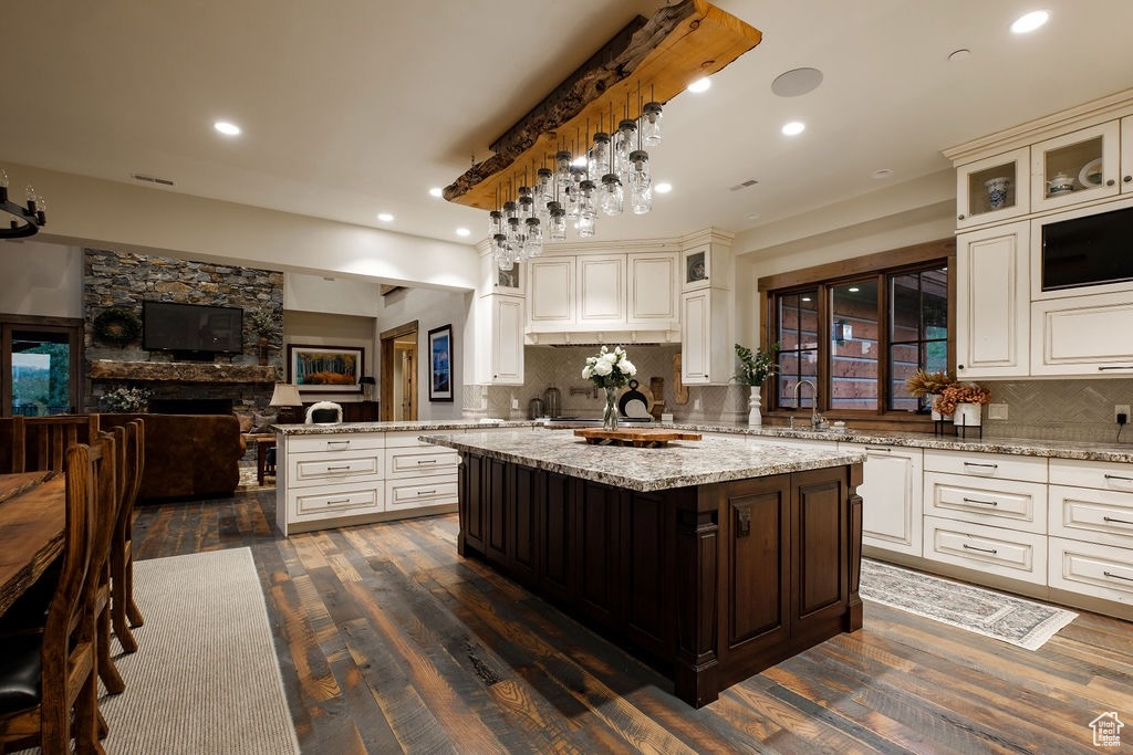 Kitchen with a stone fireplace, decorative light fixtures, tasteful backsplash, and dark wood-type flooring