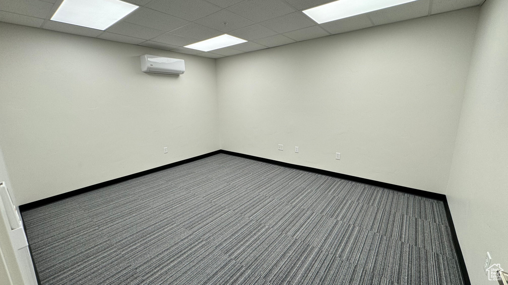Carpeted spare room with a wall mounted AC and a paneled ceiling