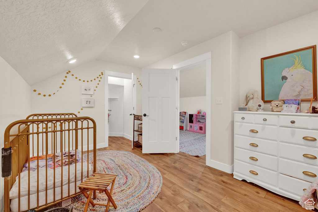 Bedroom with light hardwood / wood-style flooring, a textured ceiling, and lofted ceiling