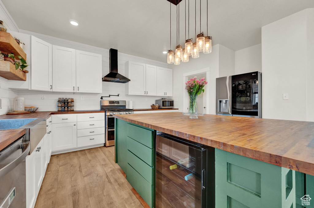 Kitchen with white cabinets, wall chimney range hood, stainless steel appliances, and wooden counters