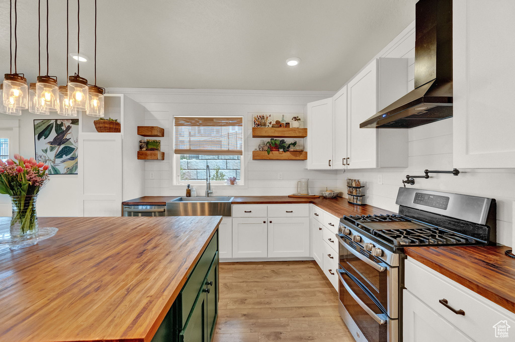 Kitchen with range with two ovens, wall chimney exhaust hood, wooden counters, and sink