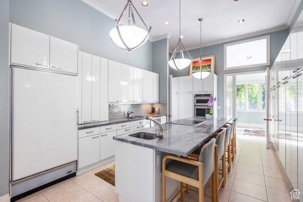 Kitchen featuring white cabinetry, a center island with sink, built in refrigerator, a breakfast bar, and sink