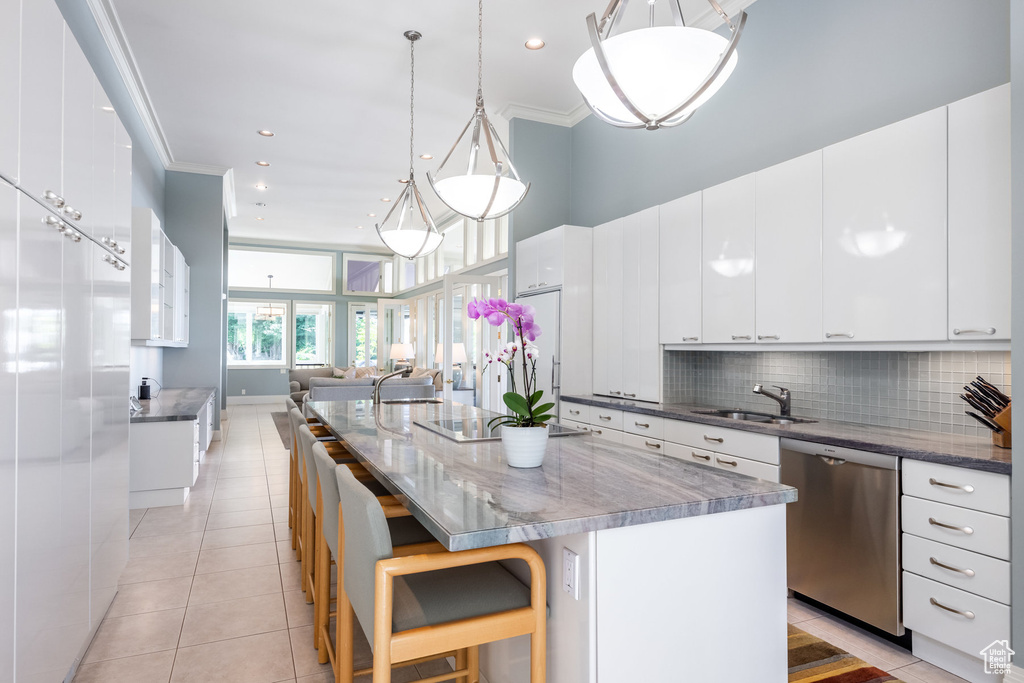 Kitchen featuring crown molding, white cabinetry, a large island with sink, dishwasher, and a kitchen bar