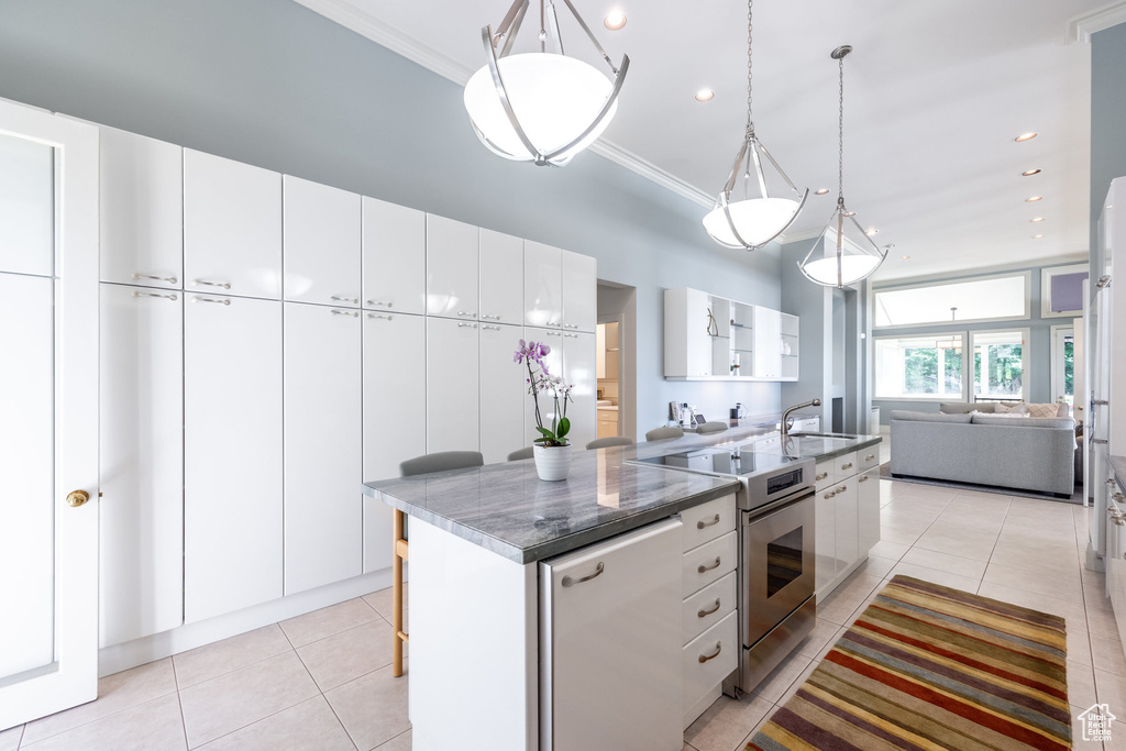 Kitchen featuring hanging light fixtures, electric range, an island with sink, white cabinets, and sink