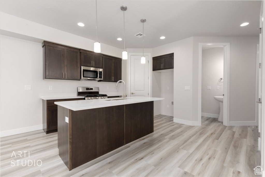 Kitchen with stainless steel appliances, an island with sink, decorative light fixtures, and light wood-type flooring