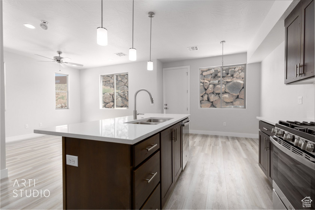 Kitchen with decorative light fixtures, light hardwood / wood-style flooring, ceiling fan, stainless steel appliances, and an island with sink