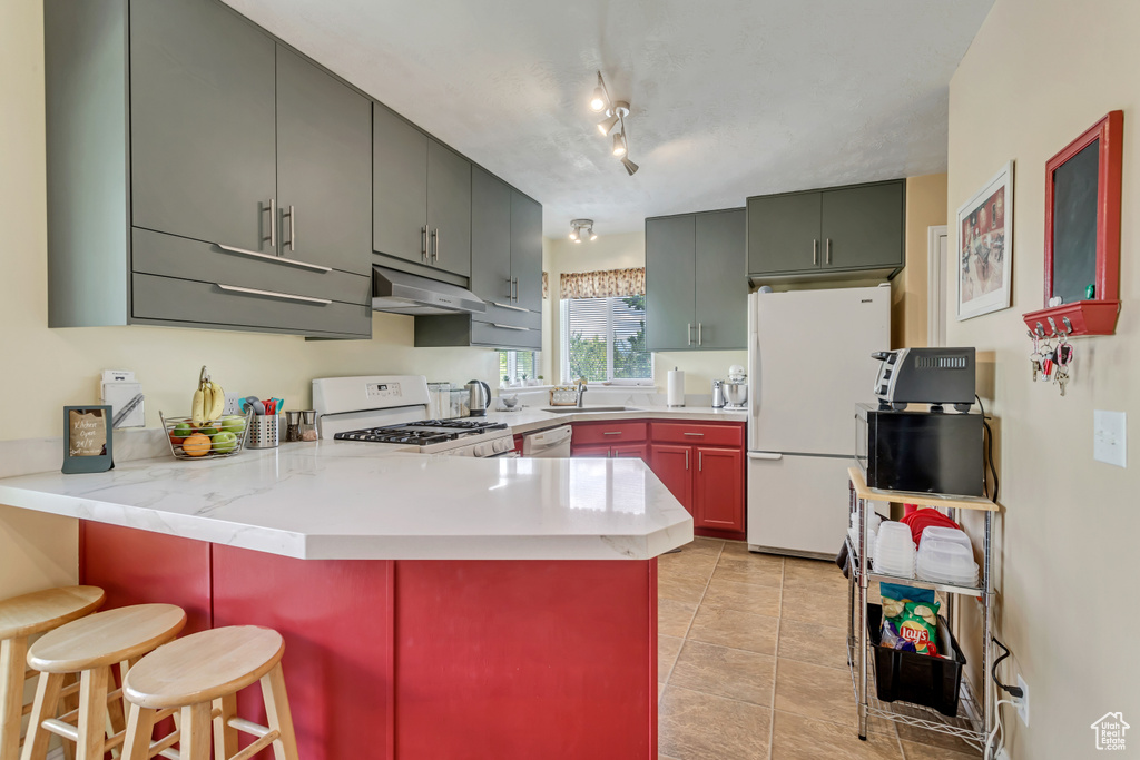 Kitchen with white appliances, rail lighting, kitchen peninsula, sink, and light tile floors