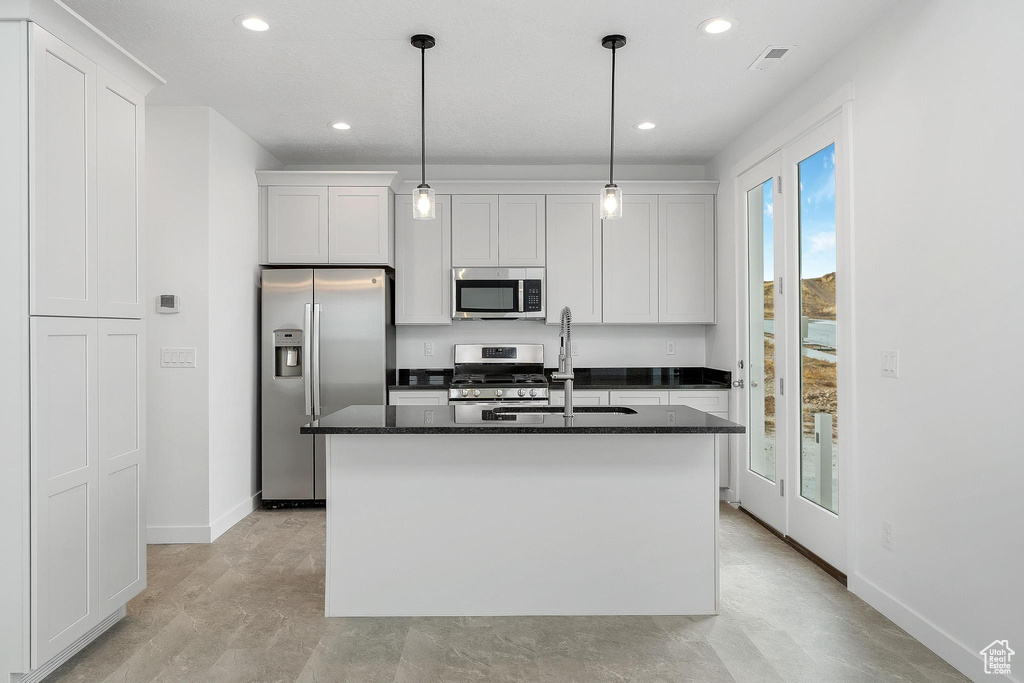 Kitchen with appliances with stainless steel finishes, a kitchen island with sink, white cabinetry, sink, and pendant lighting