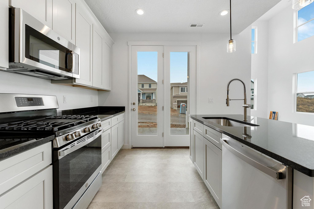 Kitchen with light tile floors, white cabinets, sink, stainless steel appliances, and pendant lighting