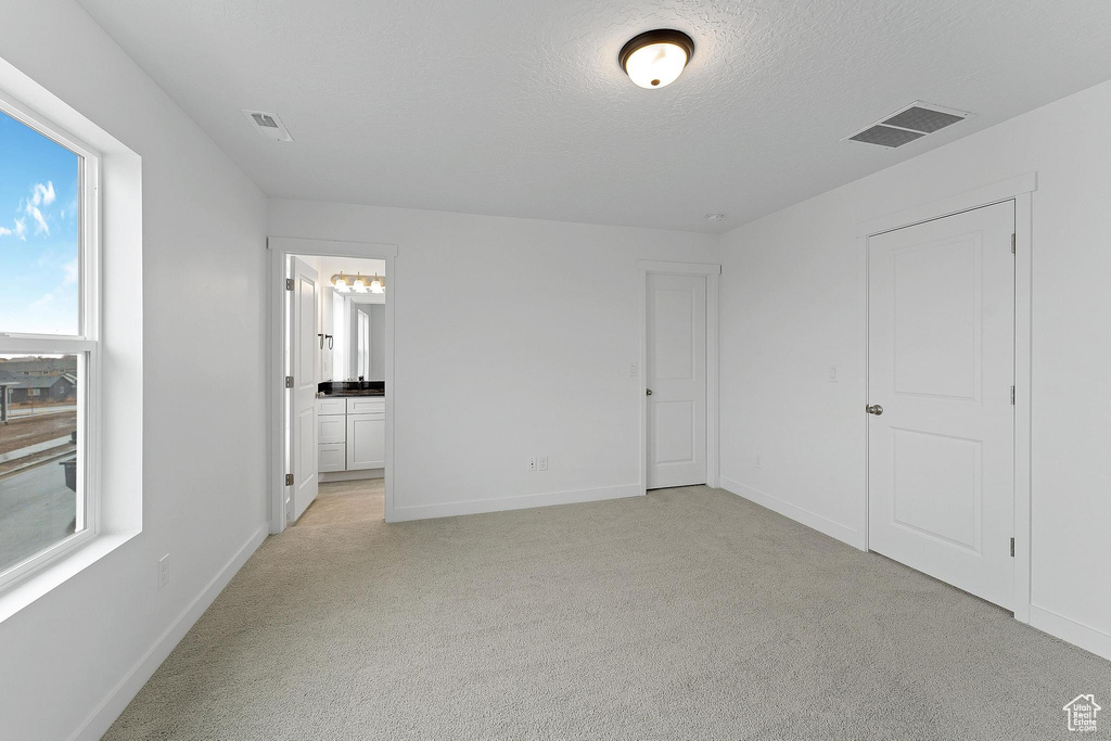 Unfurnished bedroom with light carpet, a textured ceiling, and ensuite bathroom