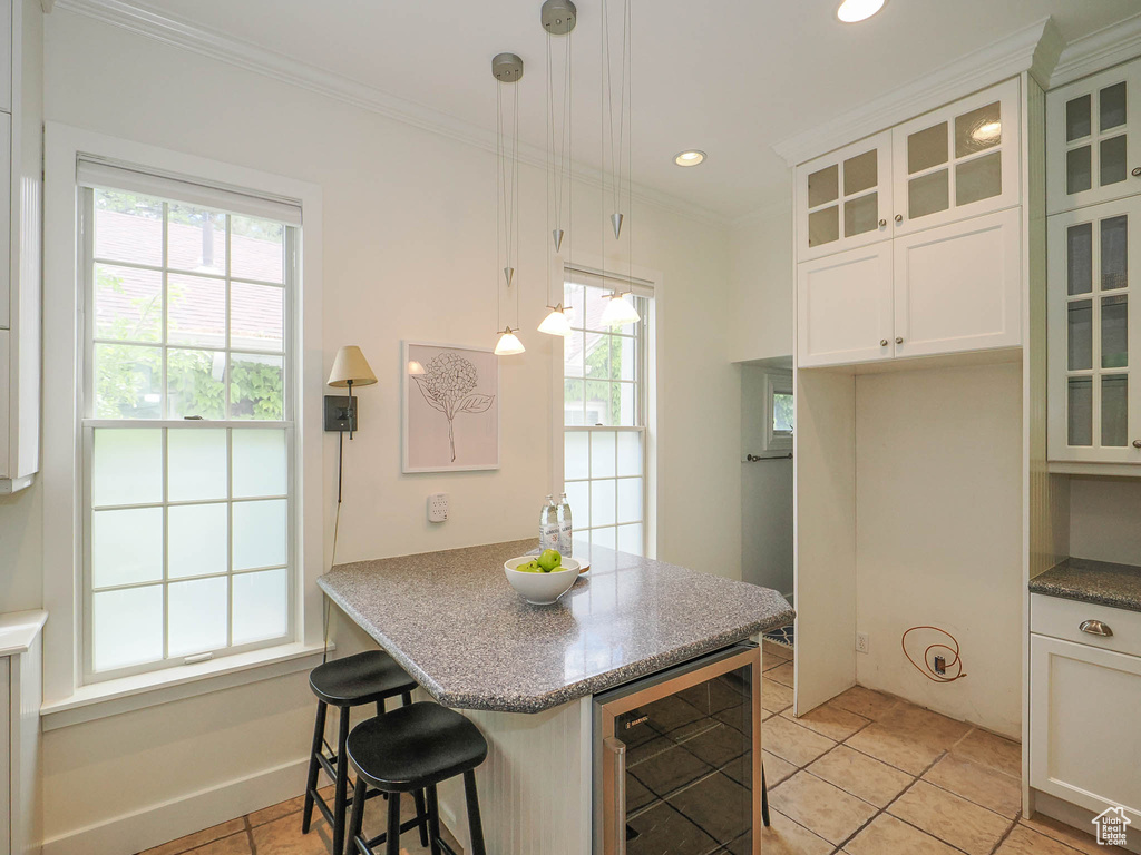 Kitchen featuring white cabinetry, decorative light fixtures, light tile floors, and beverage cooler