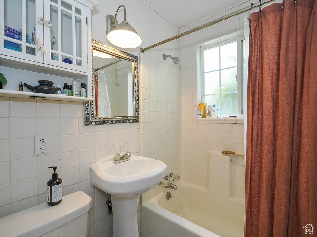 Bathroom with tile walls, toilet, and shower / bath combo with shower curtain