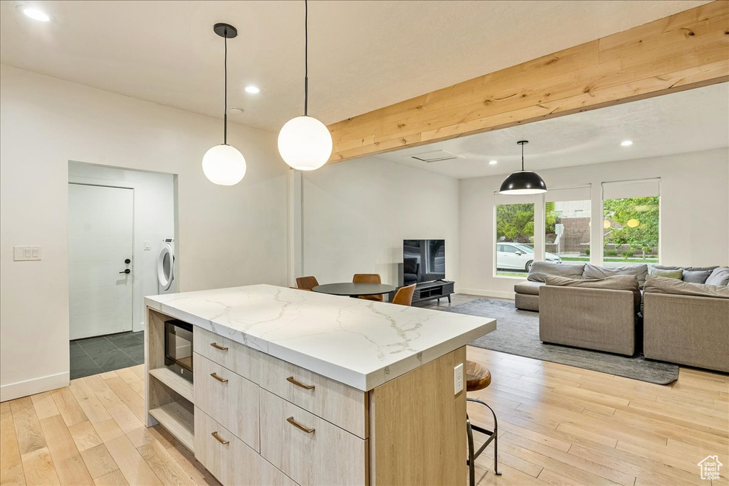 Kitchen featuring decorative light fixtures, washer / clothes dryer, light stone counters, a kitchen island, and light hardwood / wood-style floors