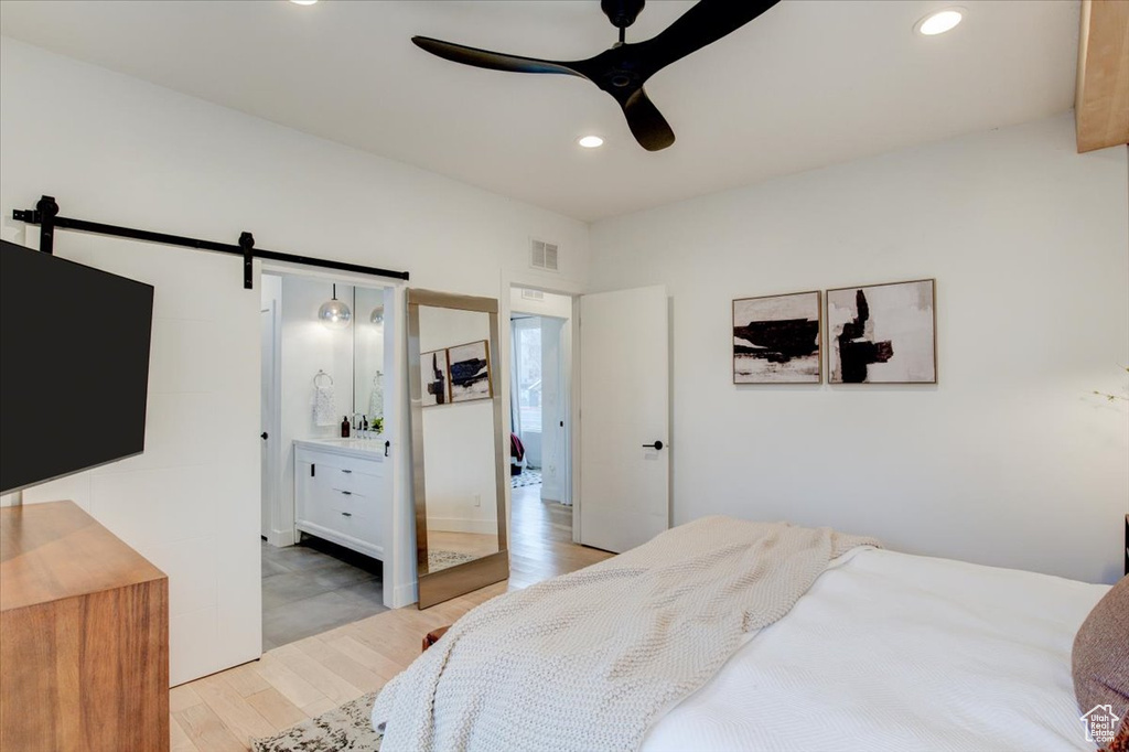 Bedroom featuring a barn door, connected bathroom, ceiling fan, and light wood-type flooring