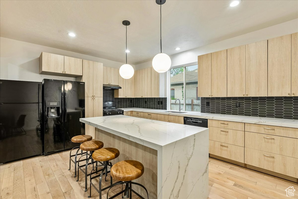 Kitchen with light stone countertops, a kitchen island, light hardwood / wood-style flooring, black appliances, and tasteful backsplash