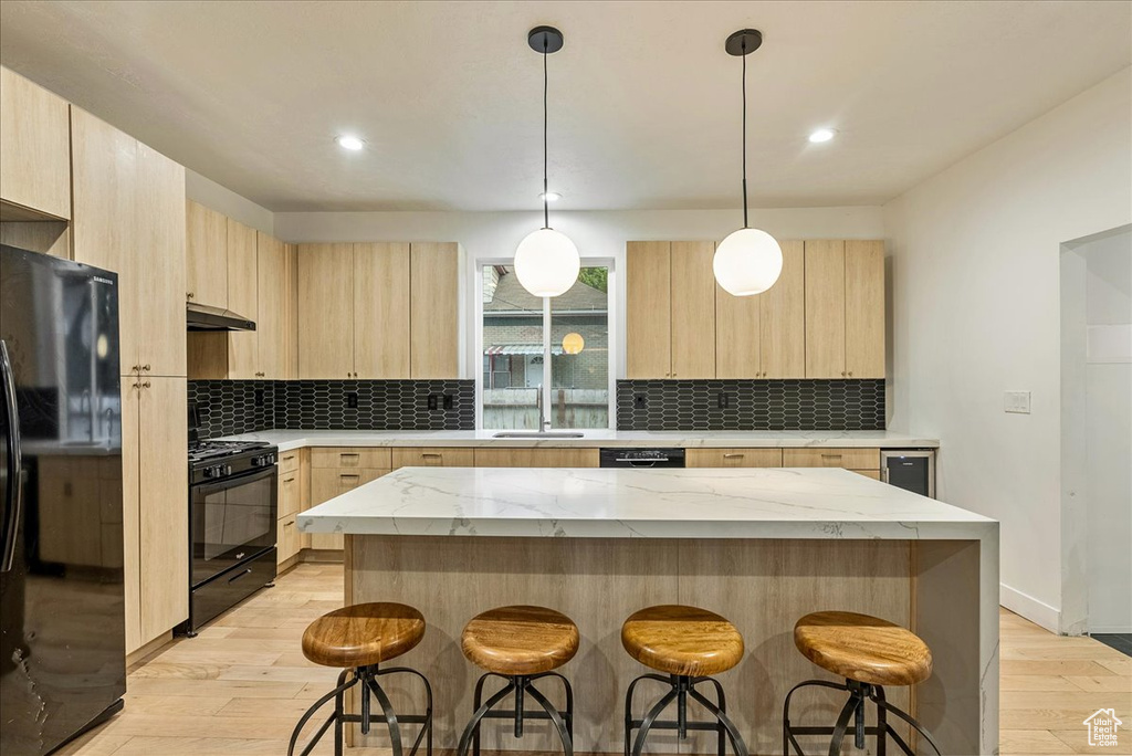 Kitchen featuring light stone counters, light wood-type flooring, a kitchen island, and black appliances