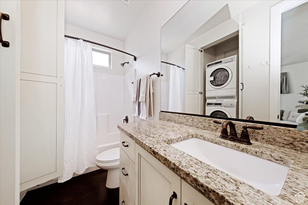 Full bathroom featuring vanity with extensive cabinet space, stacked washer / dryer, shower / bath combination with curtain, hardwood / wood-style flooring, and toilet