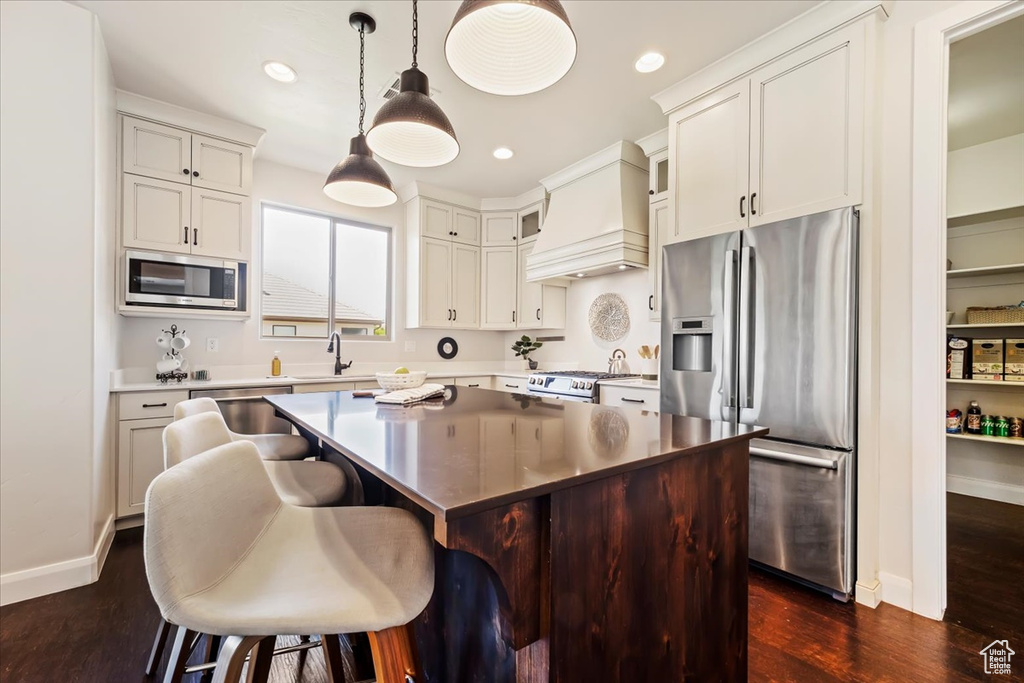 Kitchen featuring a center island, custom exhaust hood, dark wood-type flooring, stainless steel appliances, and pendant lighting
