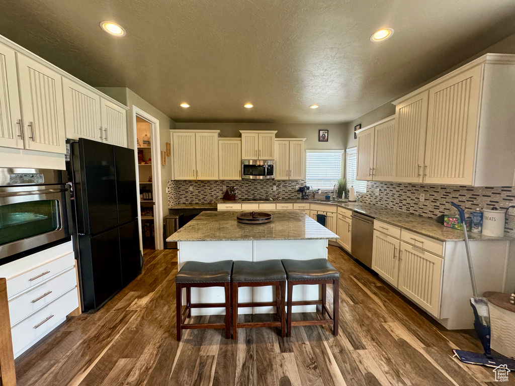 Kitchen with appliances with stainless steel finishes, a kitchen island, a breakfast bar, backsplash, and dark hardwood / wood-style floors