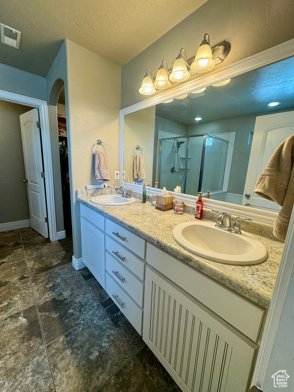 Bathroom with dual sinks, tile floors, walk in shower, and vanity with extensive cabinet space