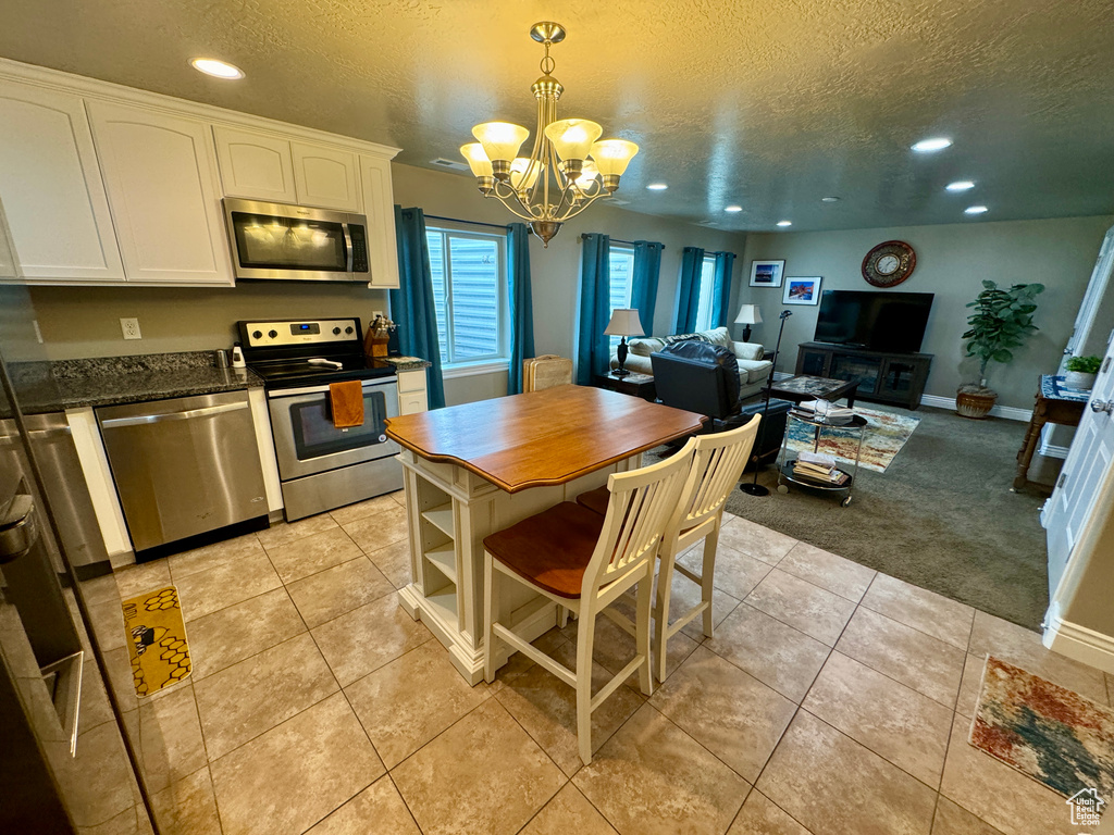 Kitchen featuring light carpet, white cabinets, decorative light fixtures, stainless steel appliances, and a notable chandelier